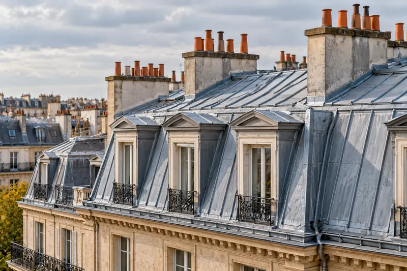 Toiture mansardée en zinc d’un immeuble ancien, avec lucarnes et souches de cheminée